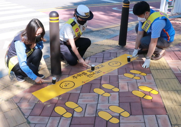 CJ대한통운 직원들이 경기도 군포시 어린이보호구역에 노란발자국을 설치하고 있다.